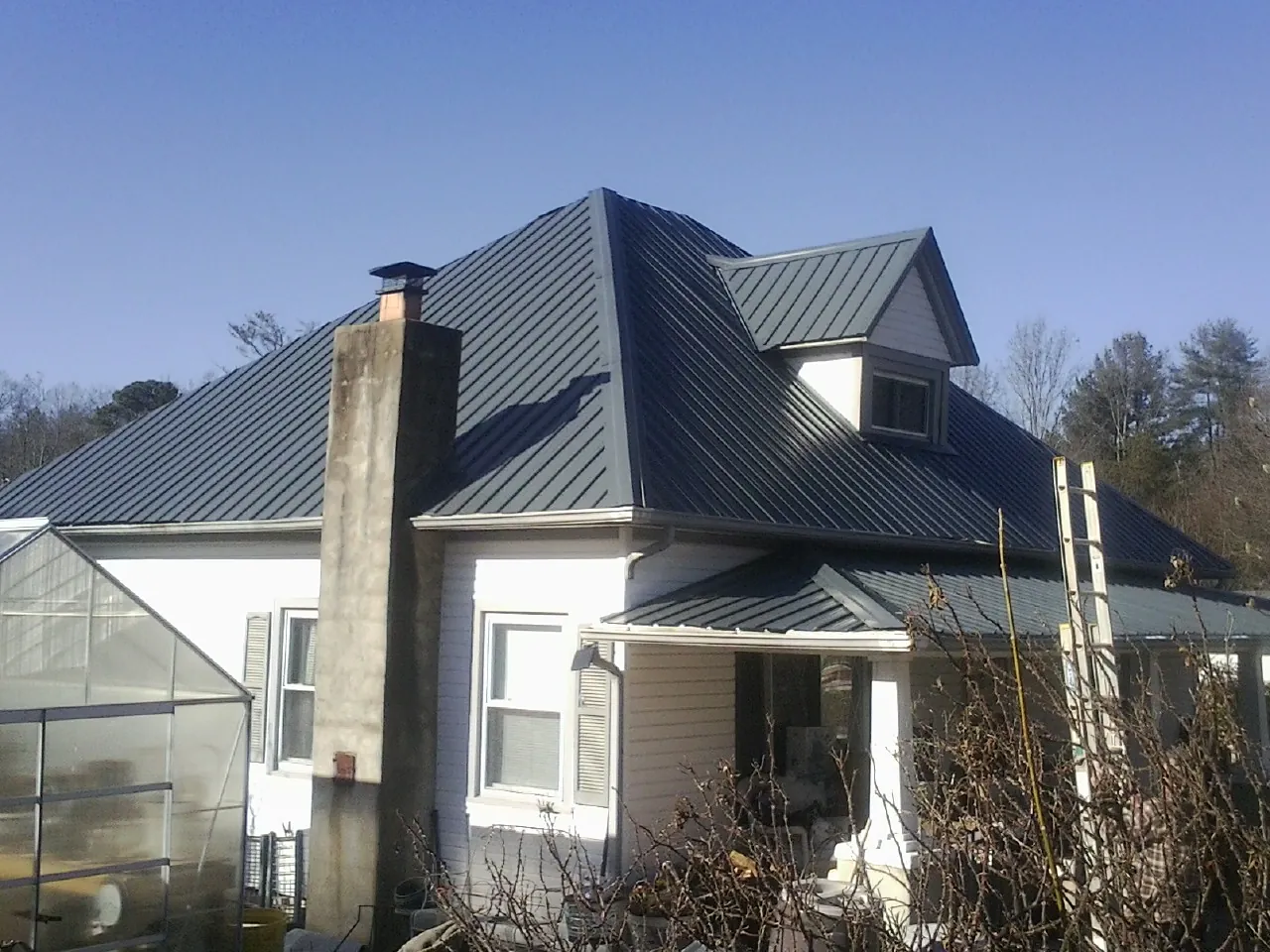Dark blue standing seam metal roof on a white farmhouse with dormer — Slate & Tile Roof Repair by Roofing Brothers in Pennellville