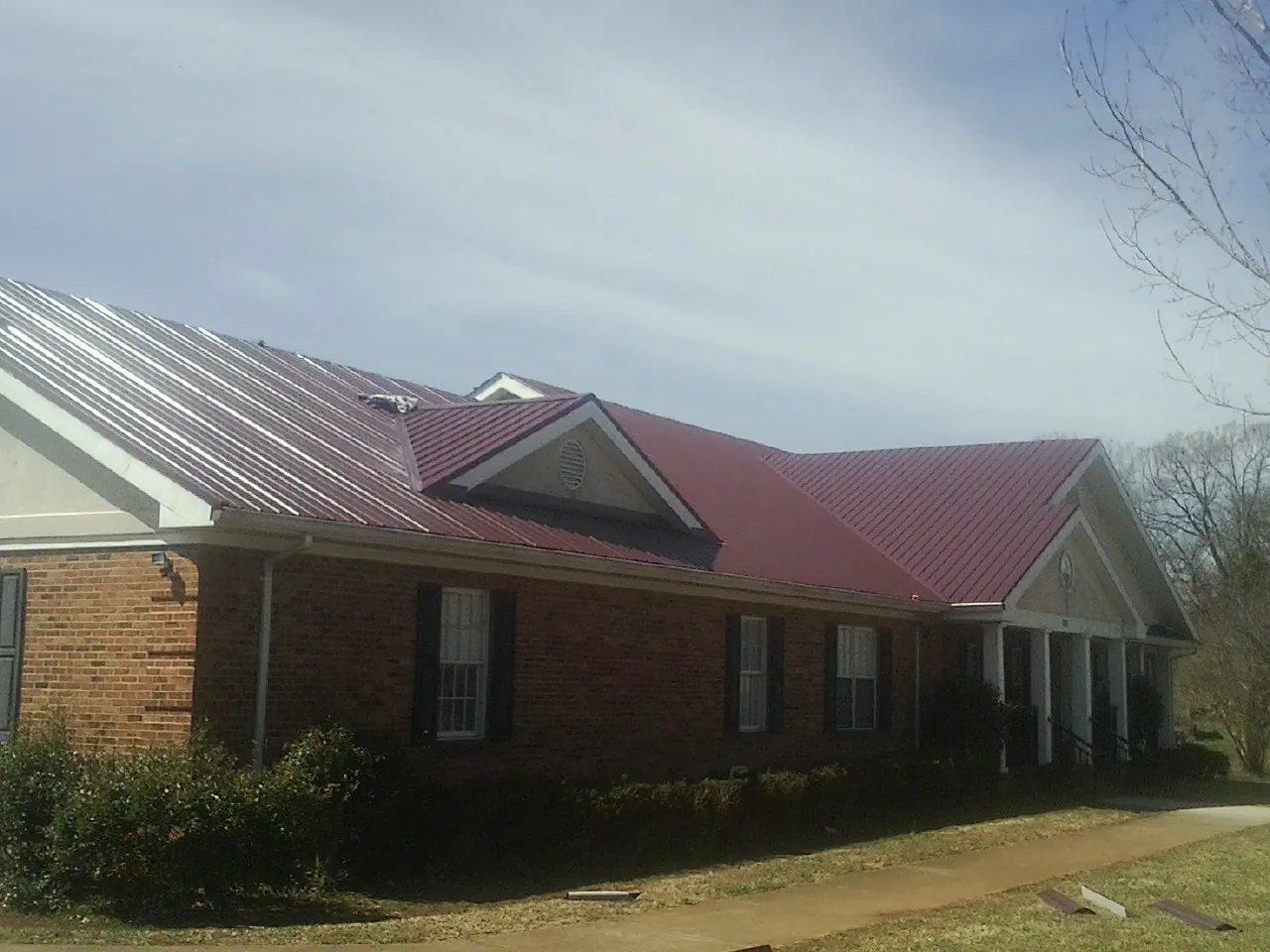 Red metal roof with gabled entries on a long brick building, from a Hail Damage Roof Repair job in Pennellville