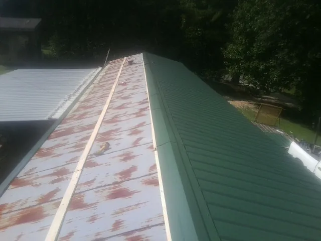 Old rusted panels beside newly installed green metal roofing — Wind Damage Roof Repair by Roofing Brothers in Pennellville