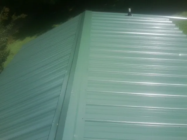 New green metal panels meeting at the ridge of a roof — Flat Roof Repair work by our crew in Pennellville