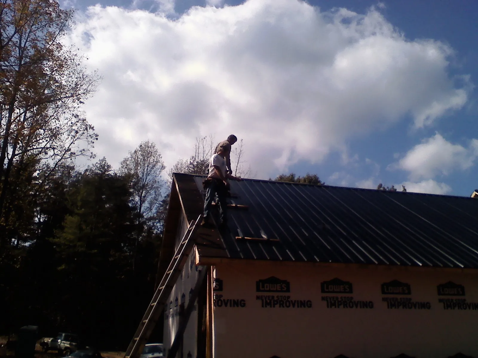 Roofer fastening dark metal panels high against a cloudy sky, from a Roof Inspection job in Pennellville