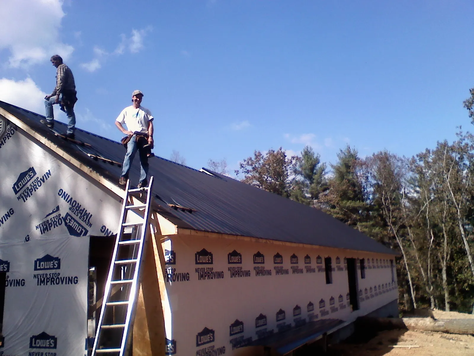 Two roofers standing on a long dark metal roof over a wrapped building in Pennellville