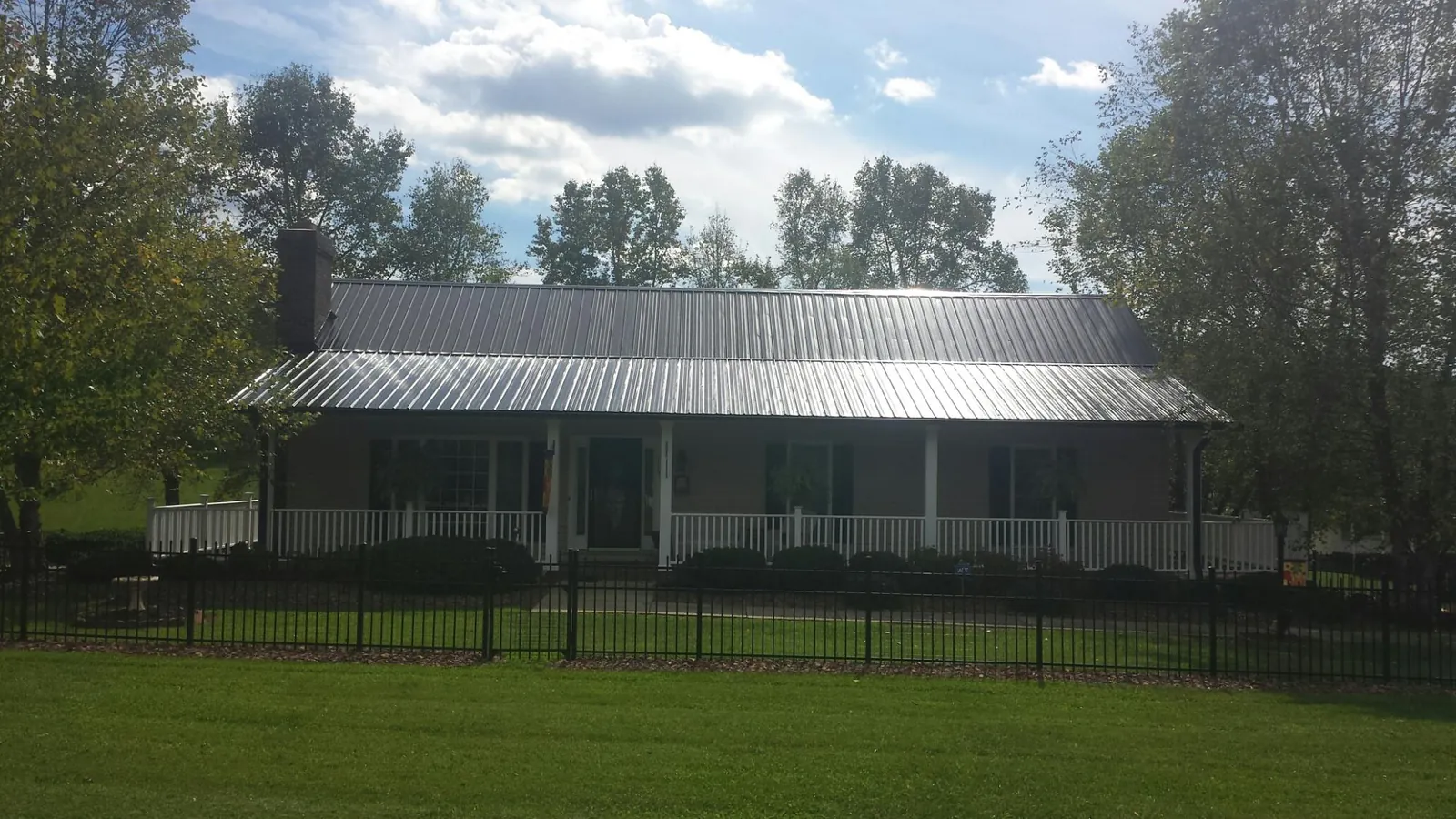 Gray metal roof on a brick ranch with a full width front porch — Gutter Guard Installation work by our crew in Pennellville