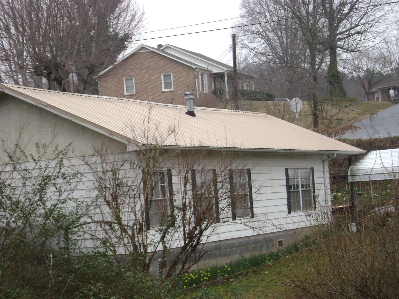 Tan metal roof on a white sided house set into a hillside — Commercial Roofing by Roofing Brothers in Pennellville