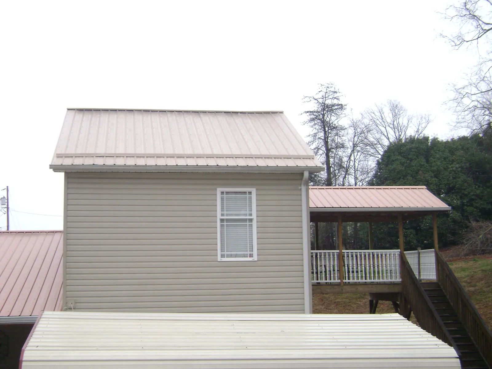 Tan metal roofs on a two story addition and attached porch, from a Roof Replacement job in Pennellville